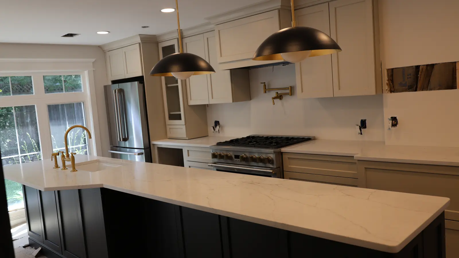 Finished kitchen with a navy island, quartz worktops, brass tapware and bronze dome pendants